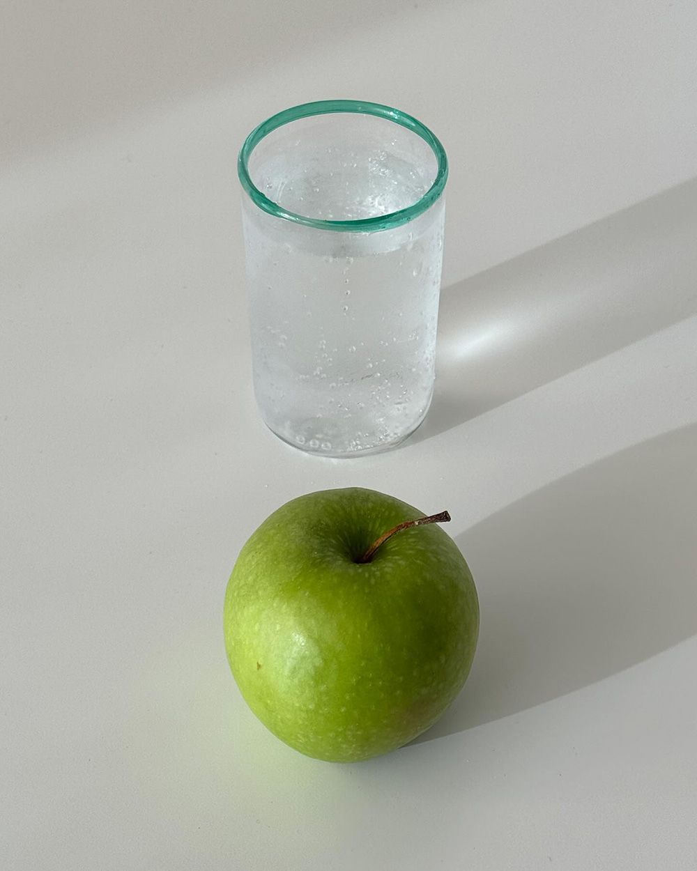 Green-rimmed glass beside a green apple in afternoon sunlight