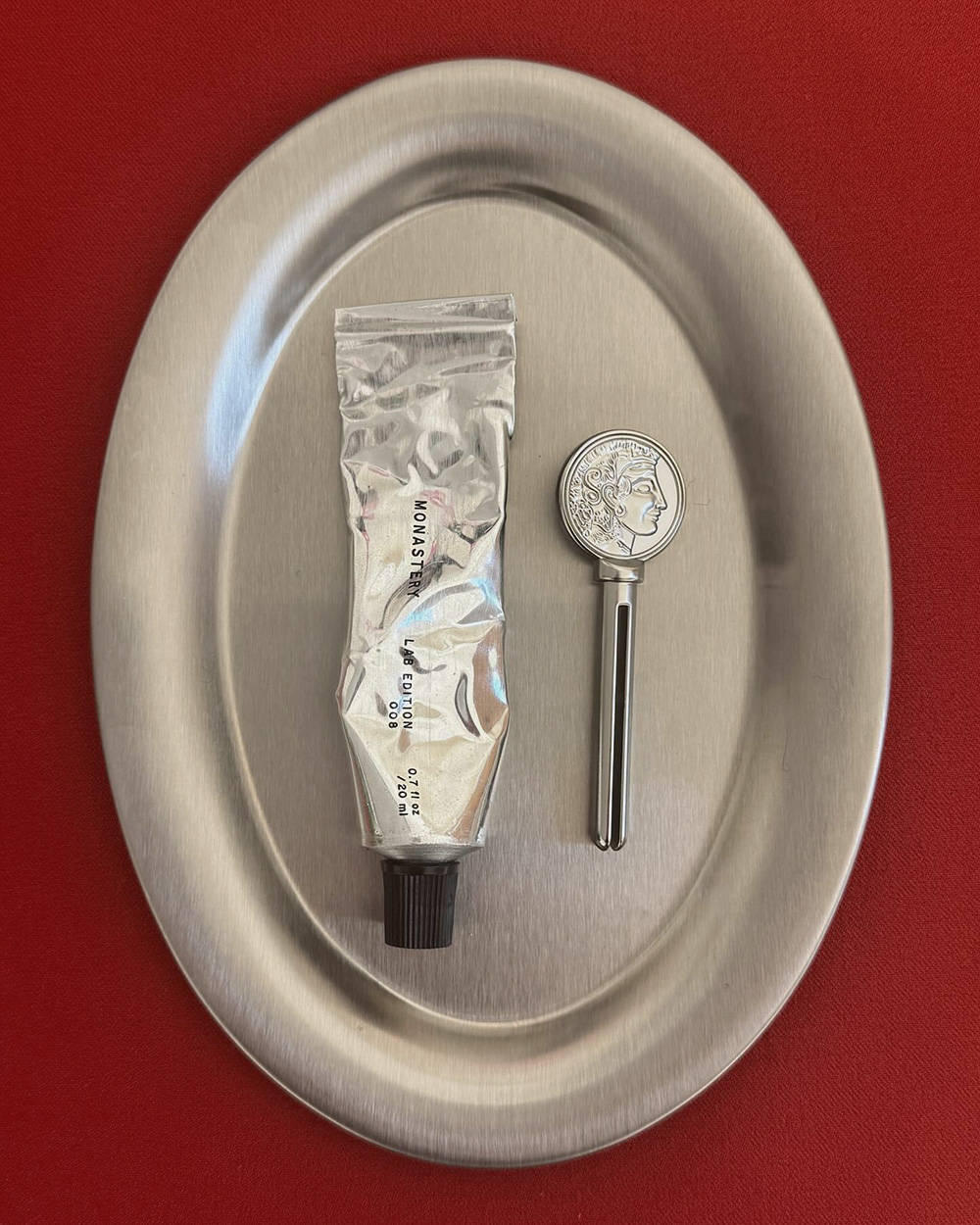 Oval silver tray with a tube and spoon against a red background
